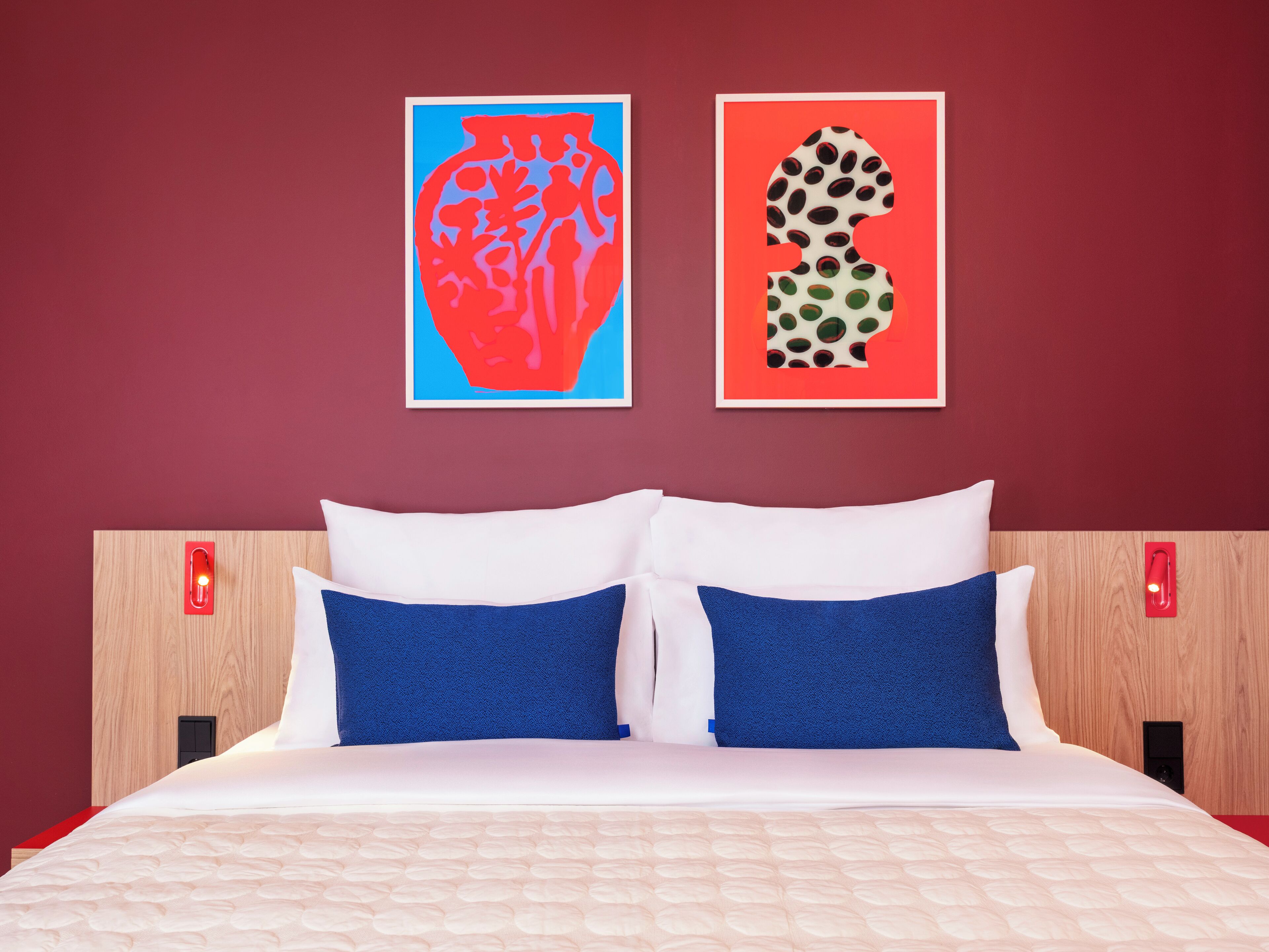 Habitación de hotel con una cama, dos almohadas, un cabecero y dos interruptores de luz en la pared.