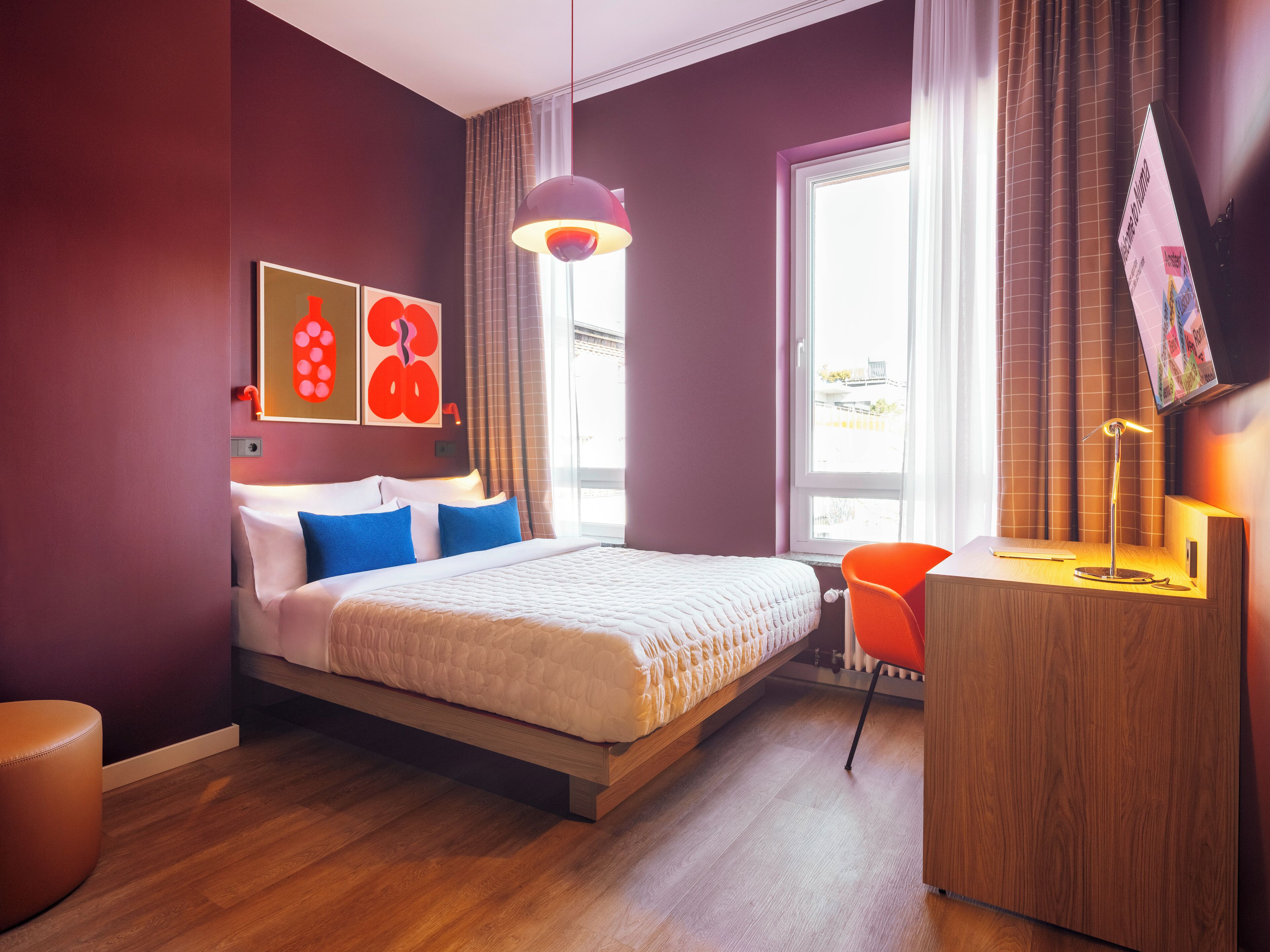 Habitació d'hotel moderna amb llit, escriptori, cadira, televisió i obra d'art a la paret.
