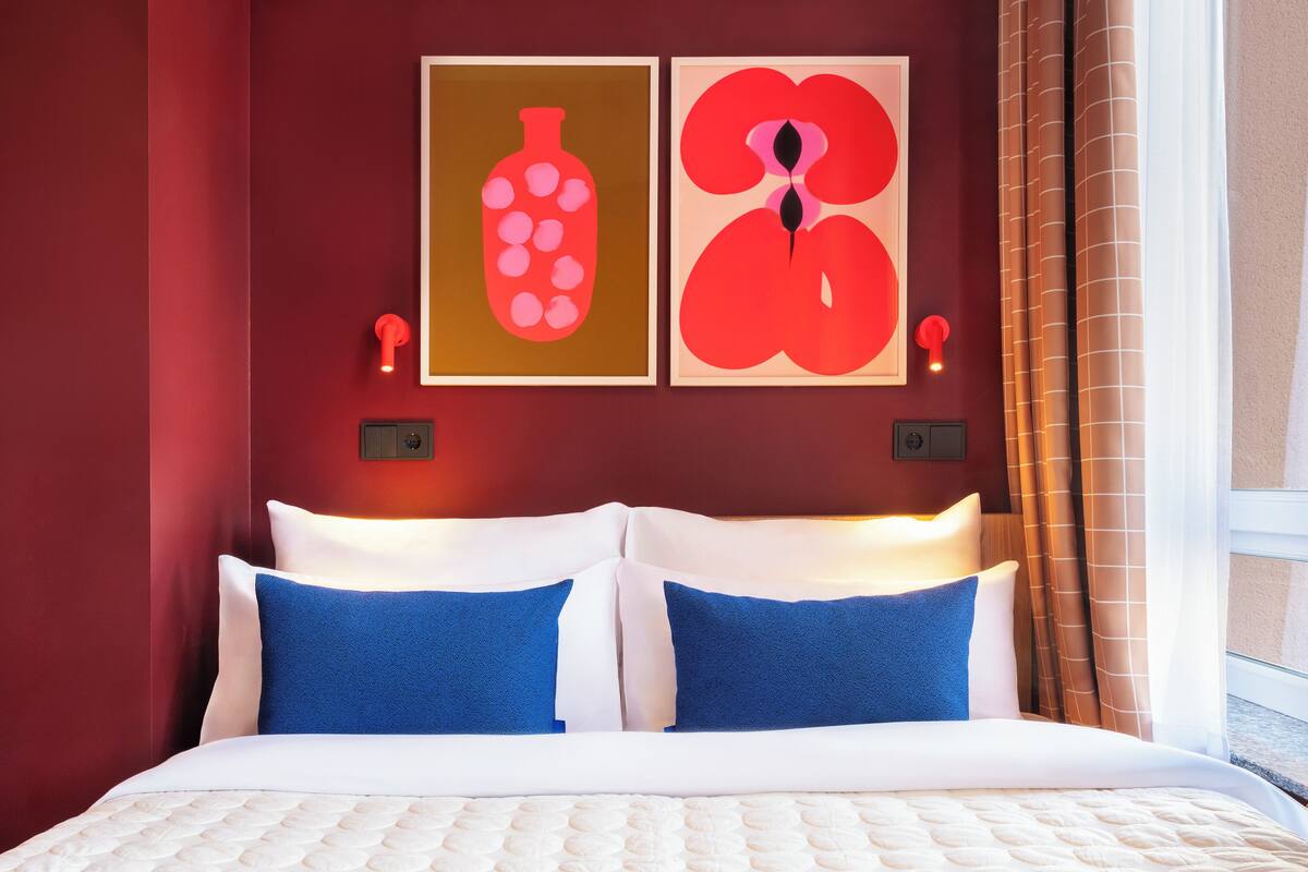 Habitación de hotel con una cama grande, dos almohadas, cabecero y dos interruptores de luz en la pared.