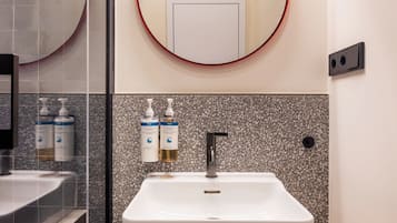 Un bagno con un lavandino bianco, due erogatori di sapone per le mani, uno specchio con cornice rossa e un interruttore della luce montato a parete.