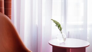 Una habitación moderna con un sillón de cuero, una mesita redonda con un florero de follaje y cortinas translúcidas.