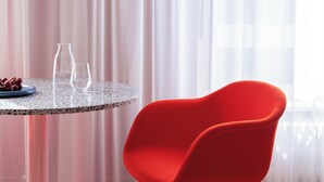 Una habitación con una mesa redonda, una silla roja y una jarra de vidrio.