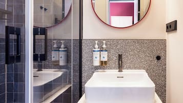 A modern bathroom with a white sink, two round mirrors, and toiletries on the wall.