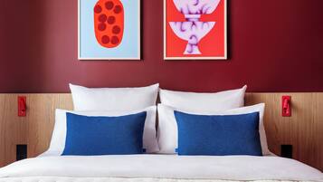 Ein Hotelzimmer mit einem Bett, zwei Kissen, einem Kopfteil und zwei an der Wand befestigten Kunstwerken.