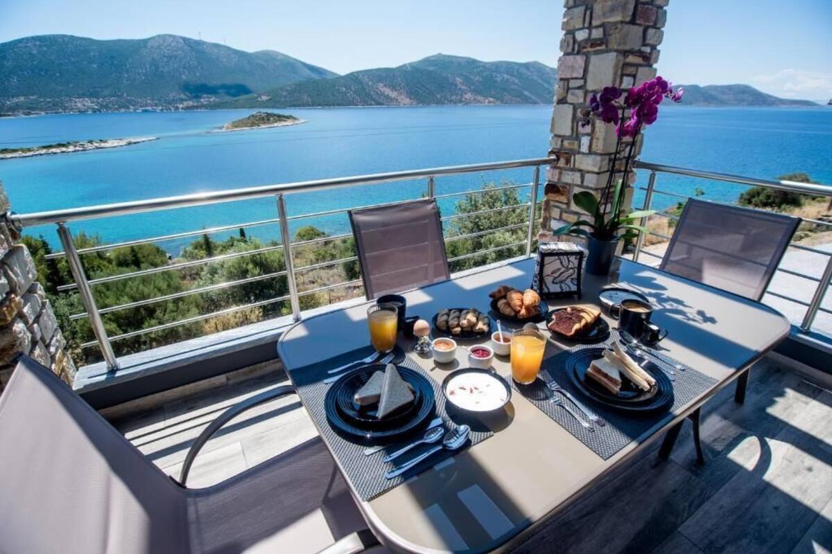 A dining table set with breakfast items, including eggs, toast, and fruit, overlooking a scenic coastal view.