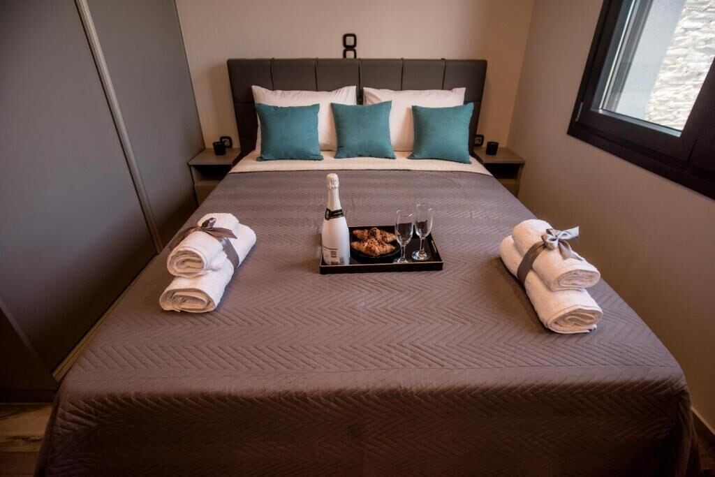 A neatly made bed with a tray of breakfast items, including a bottle, glasses, and pastries, and two towels on either side.