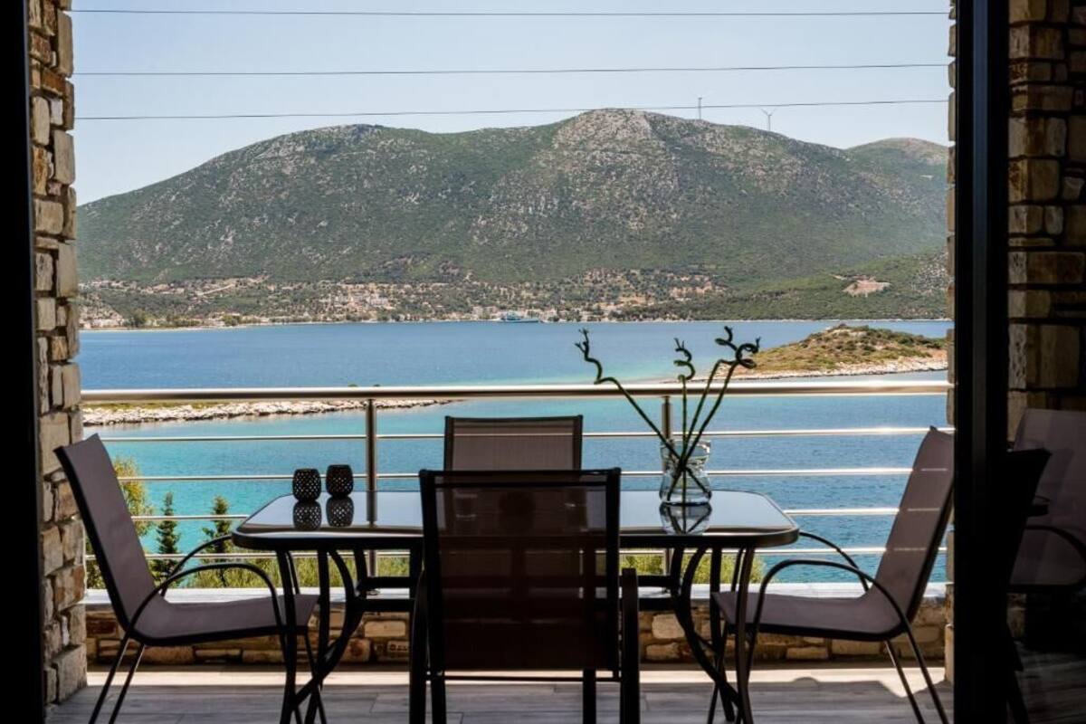 A balcony with a table and chairs, overlooking a coastal landscape with mountains and a body of water.