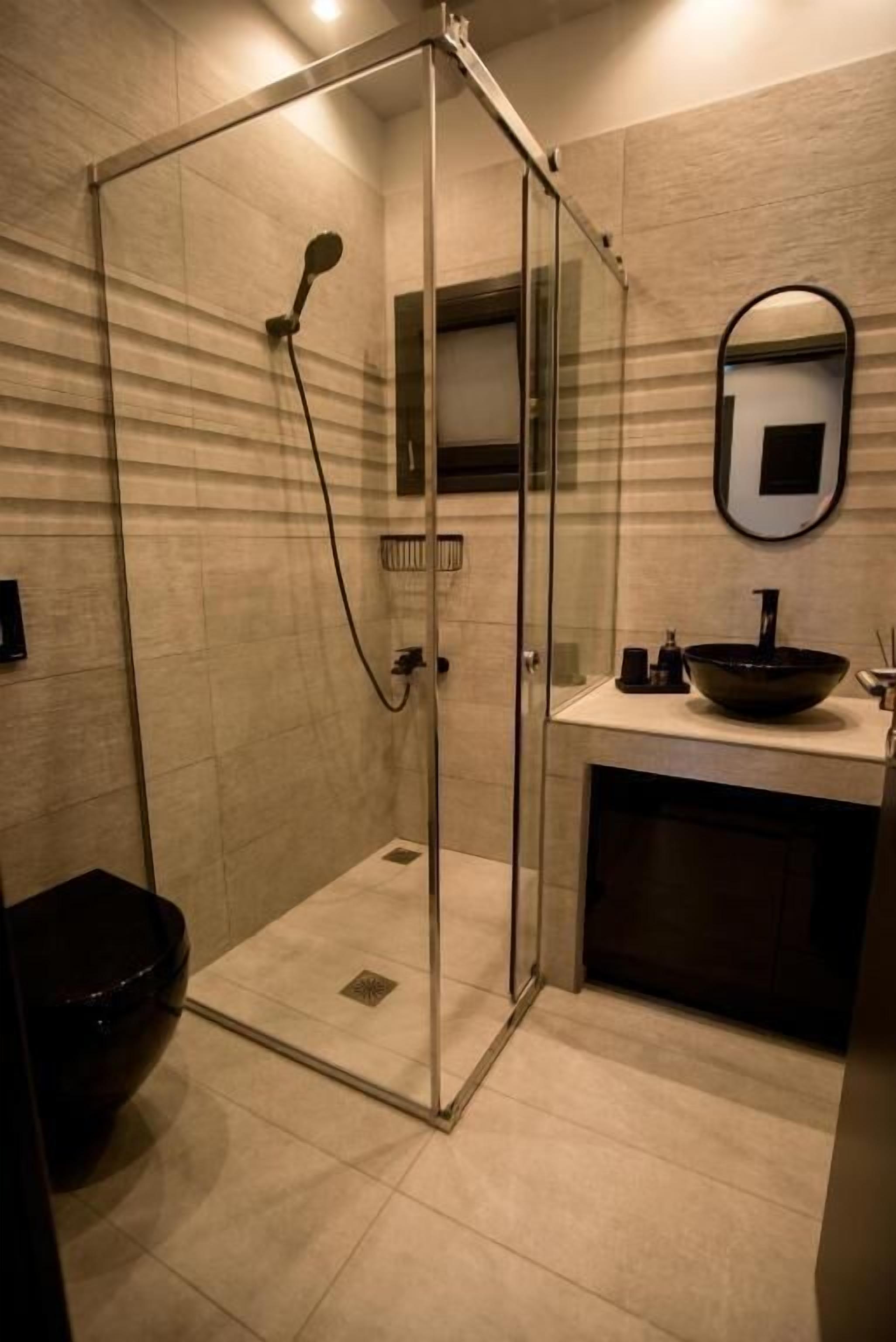 Une salle de bain moderne avec une douche à parois de verre, un miroir rond et un lavabo noir.