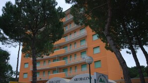 A multi-story building with balconies, surrounded by trees. - Charming apartment in the city core (Lignano Sabbiadoro)