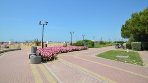 A paved walkway with a playground, a bike path, and a beach in the background. - Cozy apartment in a quiet area of Bibione (Bibione)