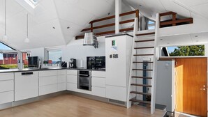 Une cuisine moderne avec des armoires blanches, un four encastré et un réfrigérateur. Un escalier en bois mène à un niveau supérieur.