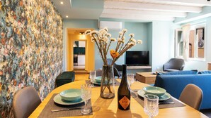 Un coin repas avec une table dressée pour quatre personnes, un vase contenant des fleurs séchées et une bouteille de vin.
