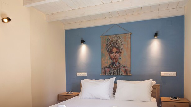 Une chambre d’hôtel avec un grand lit, deux tables de chevet, un tableau au mur et deux lampes fixées au mur.
