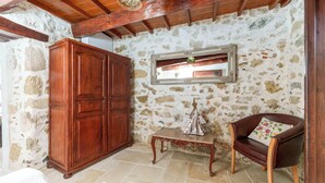 A room with a stone wall, wooden wardrobe, a small table, and a leather chair.