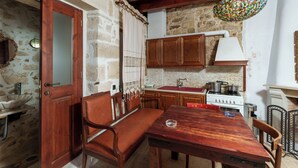 A rustic kitchen with stone walls, wooden cabinets, a bench, and a stove.