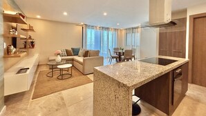 Uma sala moderna com sofá, mesa de centro e área de jantar com cadeiras. Há também uma cozinha com bancada e armários.
