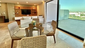 Uma sala de estar moderna com uma mesa de jantar de vidro, cadeiras de vime, um sofá e uma televisão.