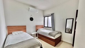 A hotel room with two beds, a bedside table, a mirror, and an air conditioning unit.