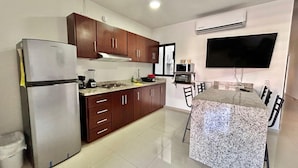 A modern kitchen with a built-in island, stainless steel refrigerator, wooden cabinets, and a flat-screen TV mounted above the island.