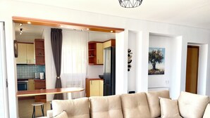 Una sala de estar con un sofá beige, una mesa de comedor de madera y una cocina al fondo.