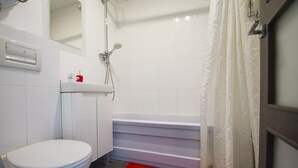 Un bany amb un vàter blanc, una banyera blanca i una catifa vermella.