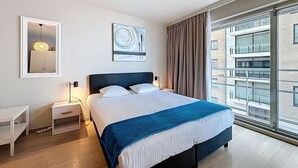 Una habitación de hotel moderna con una cama grande, mesitas de noche, un espejo, obras de arte y vistas a la ciudad.