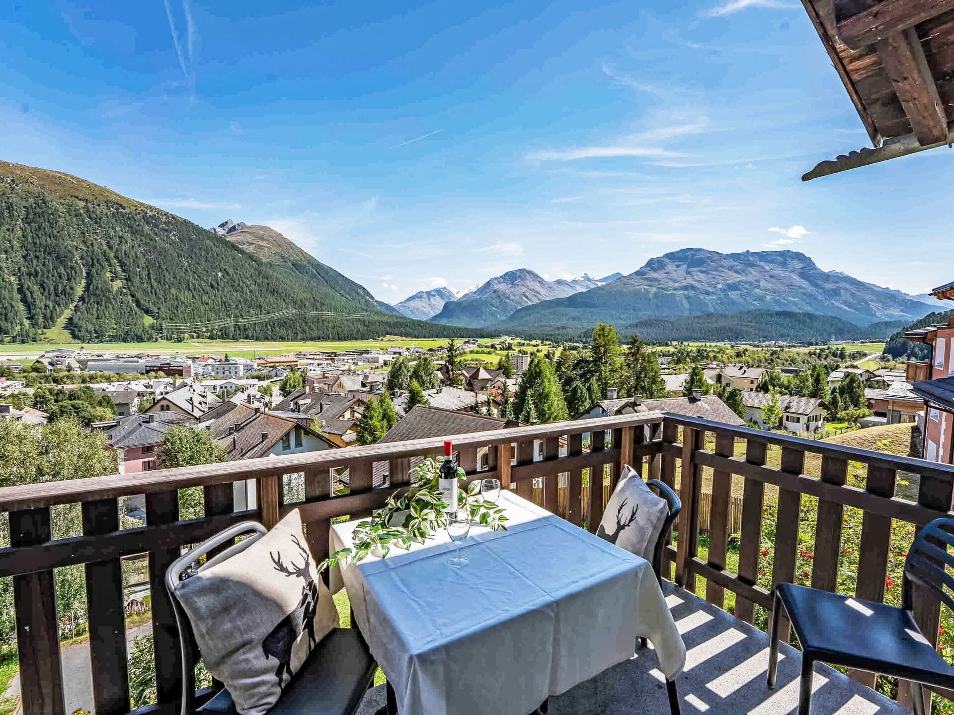 Une terrasse avec une table et des chaises, d’où l’on a vue sur un village et des montagnes.