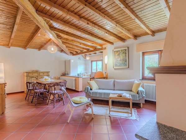 A spacious living area with a high wooden ceiling, a dining table with chairs, a sofa, and a small side table.