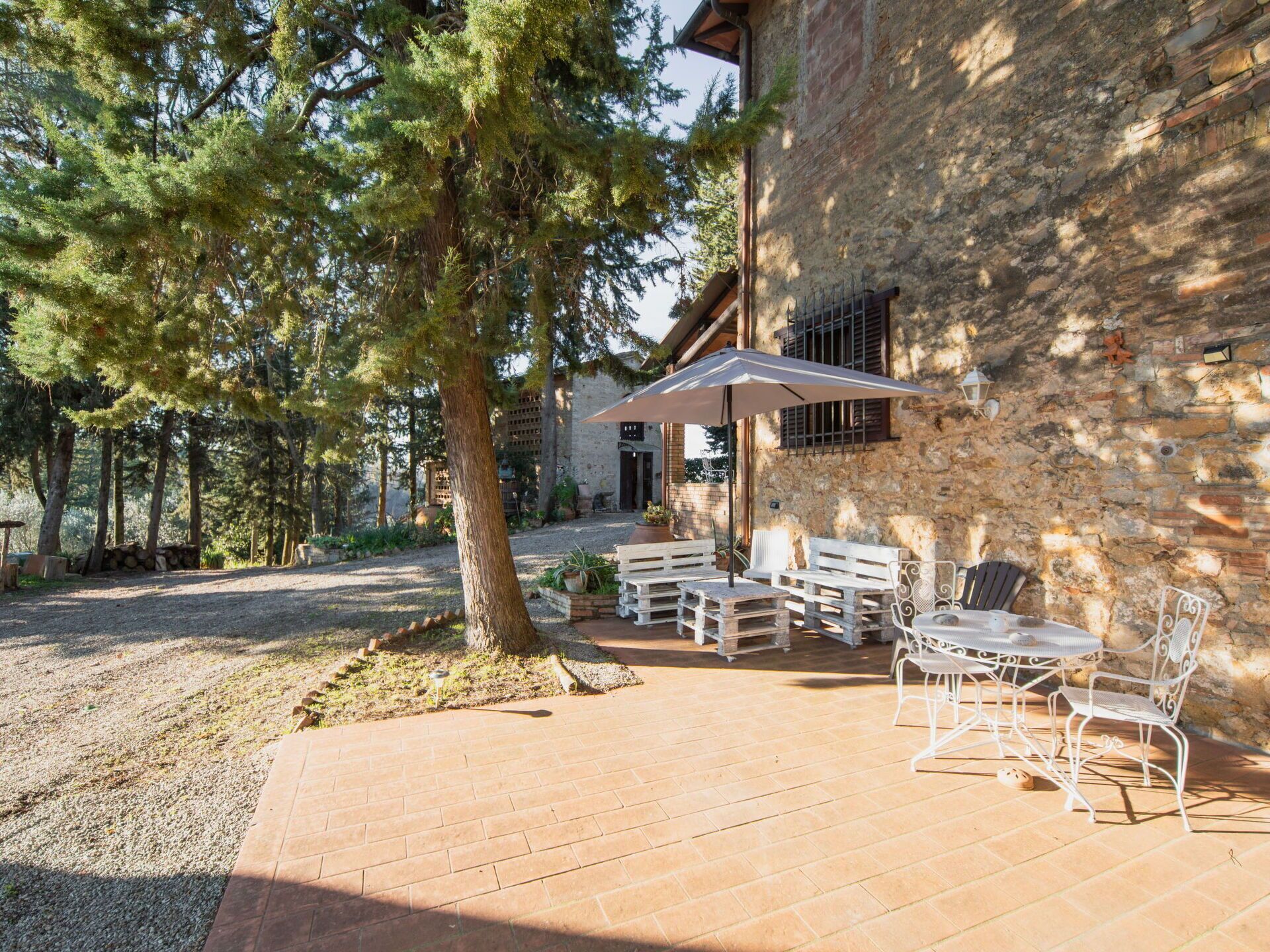 An outdoor patio with a brick floor, white metal chairs, and a table under a white umbrella.