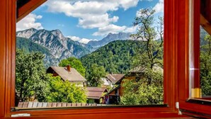 A mountain view from a window with wooden frames, featuring houses and lush greenery.