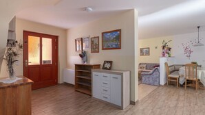 A spacious living area with a wooden floor, a red door, a white cabinet, and a dining area with a table and chairs.