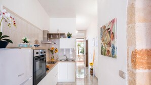 Eine moderne Küche mit weißen Schränken, einem eingebauten Ofen und einem Spülbecken. Auf der Arbeitsplatte steht ein Blumentopf und an der Wand hängt ein Gemälde.