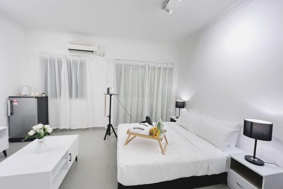 A hotel room with a bed, bedside table, lamp, and a small desk with a computer.