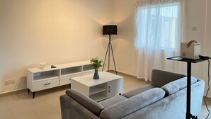 Un salon moderne avec un canapé gris, un meuble TV blanc, une lampe sur pied et un projecteur posé sur une table.