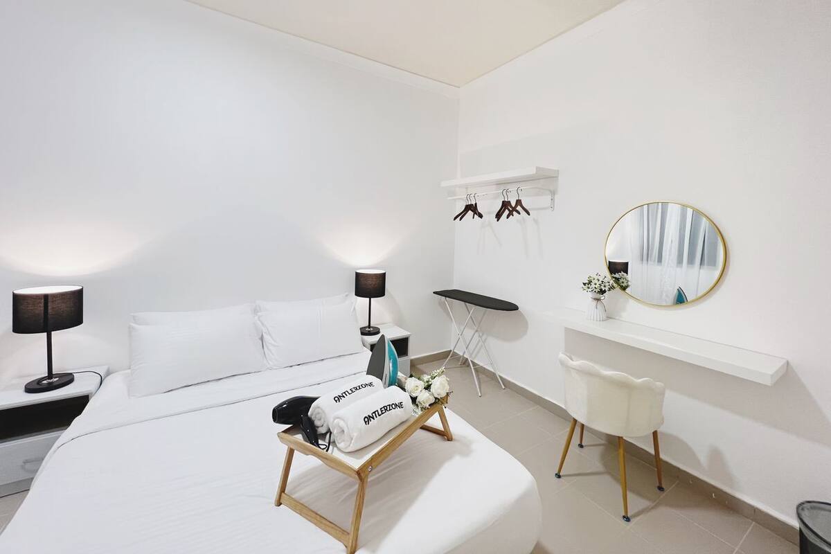 Une chambre d’hôtel moderne avec un lit bien fait, un petit bureau avec une lampe, une coiffeuse avec un miroir et une chaise.