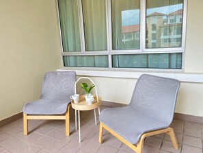 Two grey cushioned chairs with wooden legs, a small round table with a plant and two white cups, and a window with curtains. - Tiara Desaru By Antlerzone (Bandar Penawar)