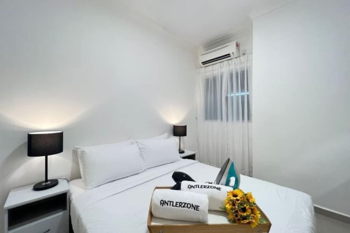 Een hotelkamer met een bed, twee nachtkastjes, een lamp, een raam met gordijnen en een decoratief object met de tekst 'ANTLERZONE'.