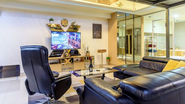 A modern living room with a black leather sofa, a glass coffee table, a black office chair, a flat-screen TV, and a decorative wall piece. - Xspa Apartment Cryptocurrency pay Available (Novi Sad)