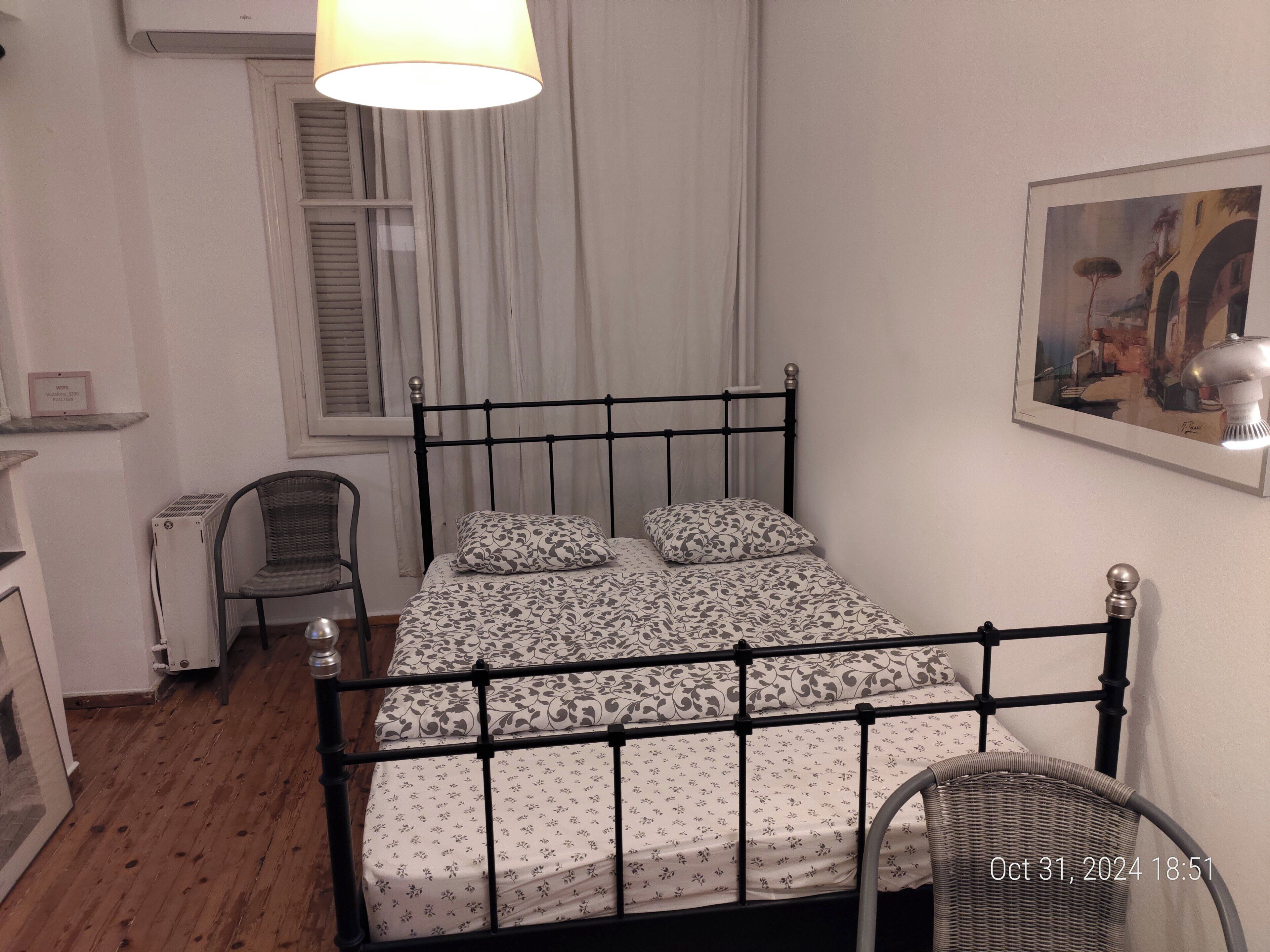 A bedroom with a bed, a chair, a lamp, a radiator, and a window with curtains.