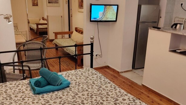 Un dormitorio con una cama, televisor montado en la pared, refrigerador y una pequeña cocina.