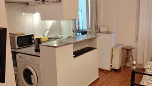 Cocina compacta con lavadora, microondas y una pequeña encimera.