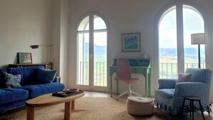 Un salon spacieux avec un canapé bleu, une table basse en bois et une vue dégagée grâce à de grandes fenêtres en arc de cercle.