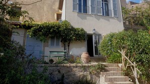 Un bâtiment à deux étages, doté d’une façade blanche, de fenêtres en arc de cercle et d’un petit porche avec des chaises vertes.