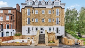 Un immeuble résidentiel à plusieurs étages, doté d’une façade en briques, de nombreuses fenêtres et d’un escalier central menant à l’entrée.