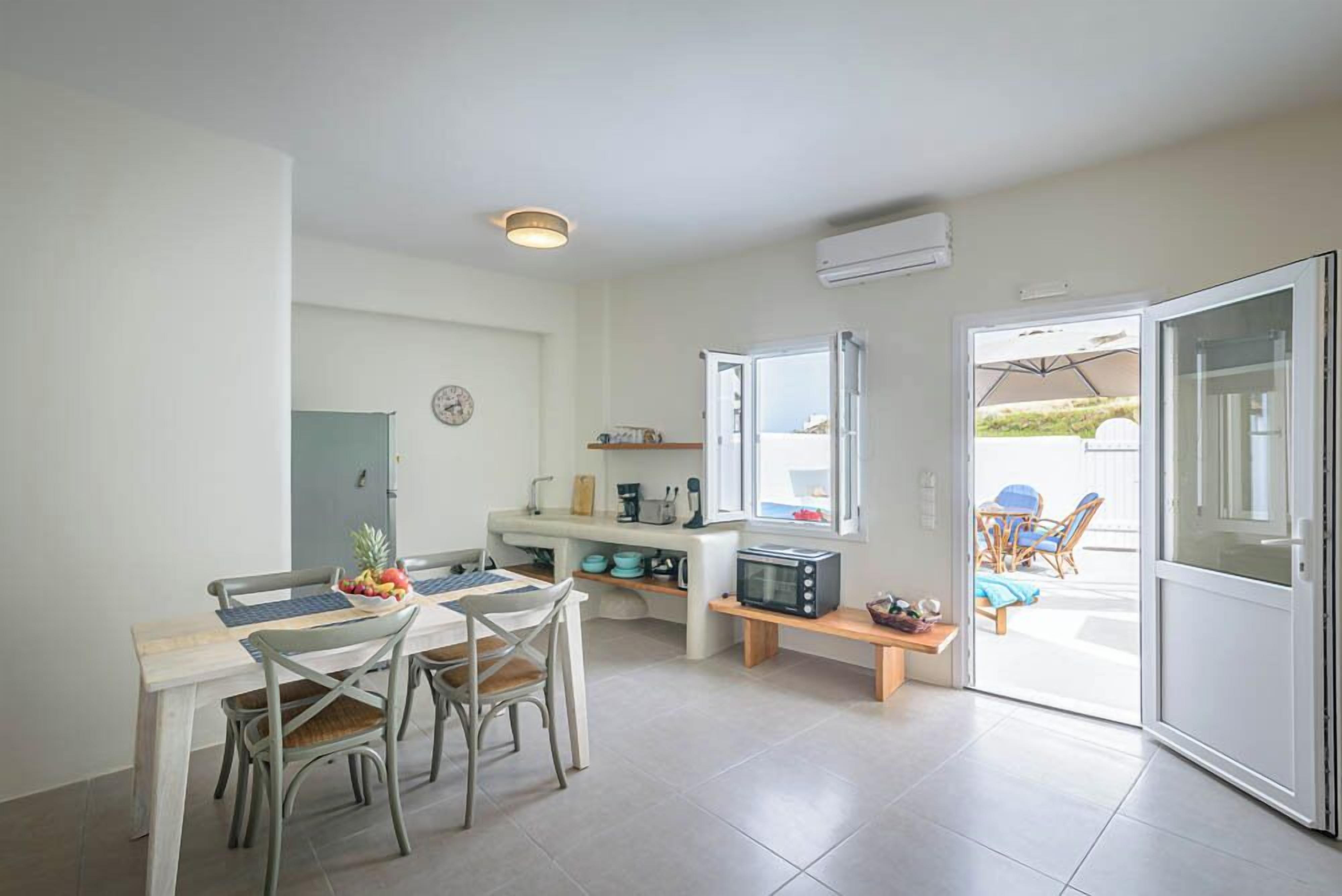 A compact kitchen with a dining area, a small table with chairs, a microwave, and a window overlooking a patio with outdoor seating.