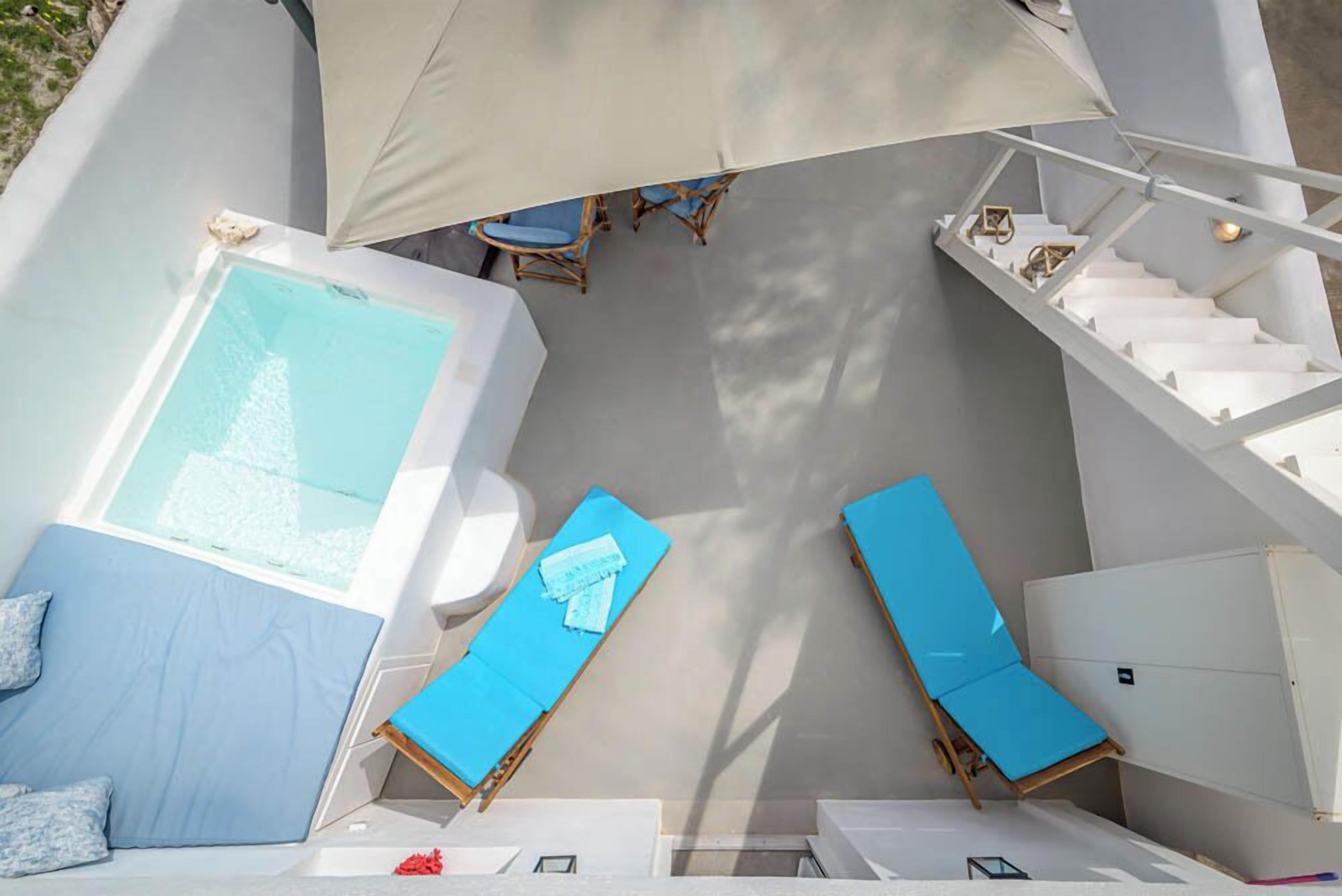 A modern outdoor lounge area with a pool, two blue lounge chairs, a small table with chairs, and a staircase leading to an upper level.
