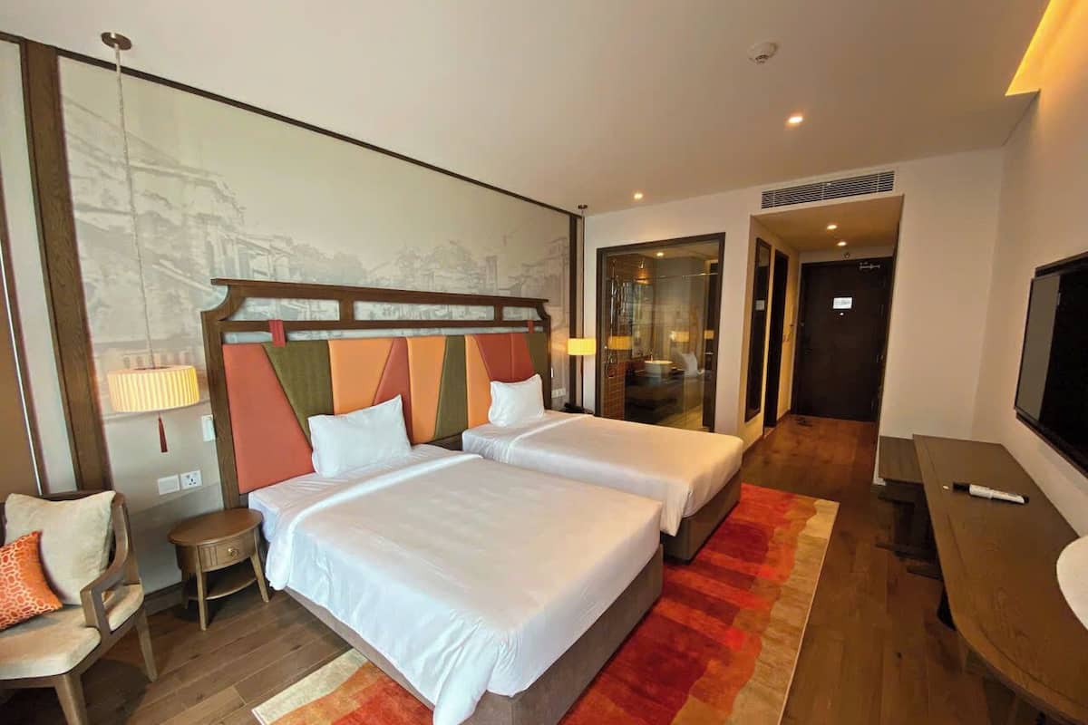 A hotel room with two beds, a desk, a chair, and a large window.