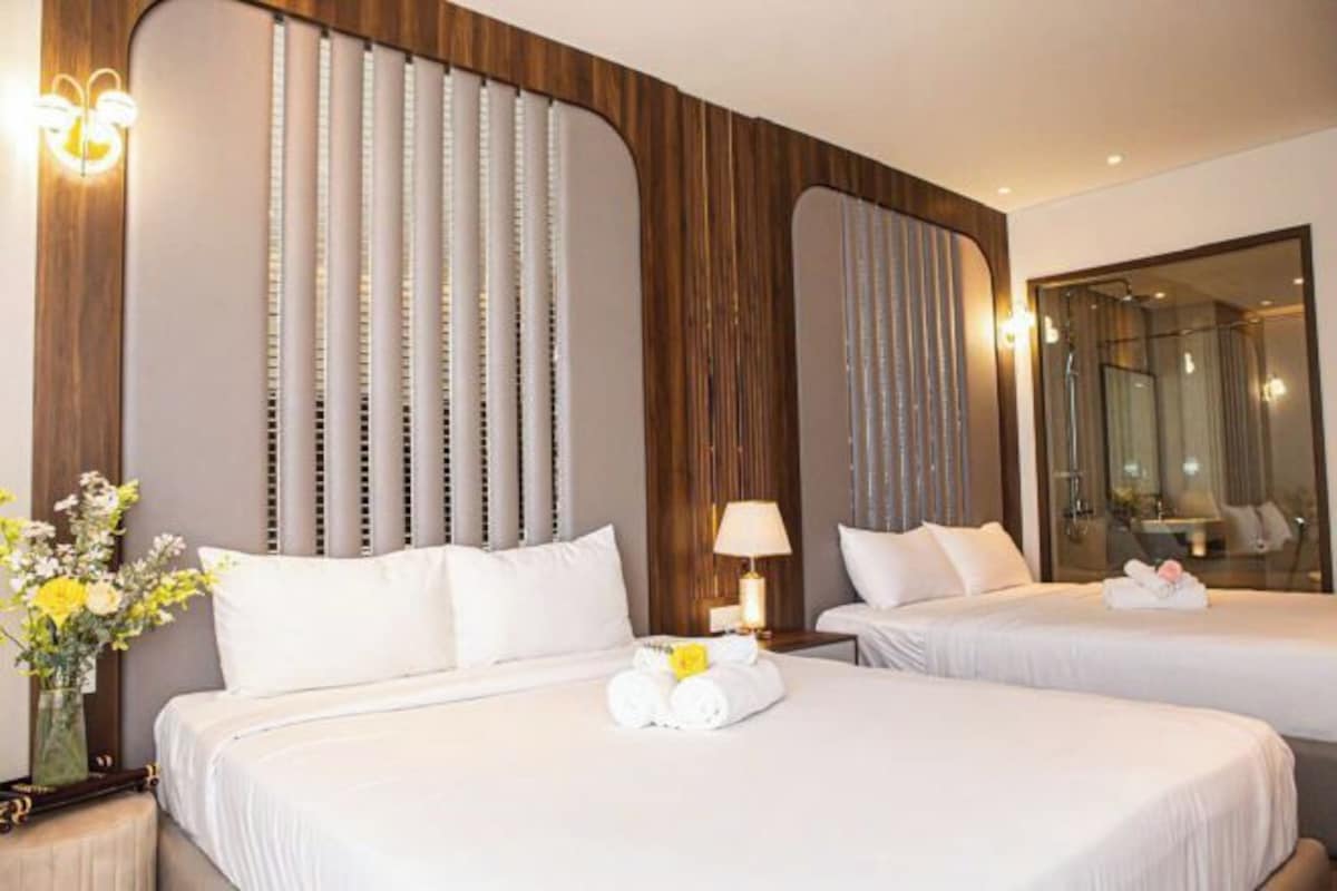 Habitación de hotel con dos camas, un espejo grande y un florero con flores.