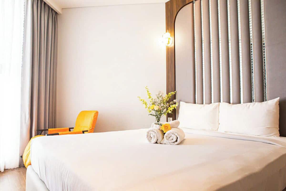 A hotel room with a large bed, a chair, and a vase with flowers.