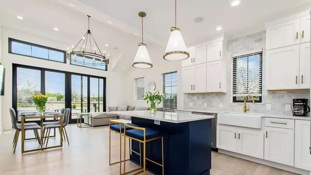 Una cocina moderna con una isla central, luces colgantes y un comedor con mesa y sillas.